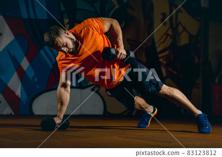 Full-length portrait of sportive man doing push-ups with dumbbells, training in sport gym 83123812