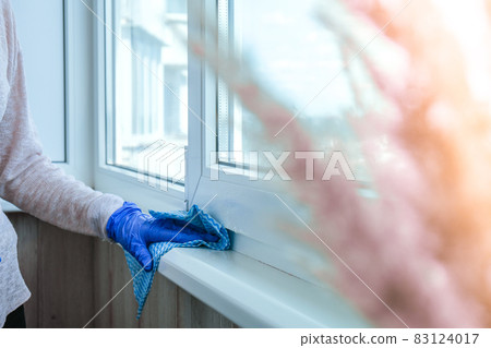 Cleaning the windowsill wiping dust by blue microfiber cloth for cleaning on the glass window rail Blue Gloves Cleaning Using Sprayed Liquid. Housework and housekeeping concept. Spring 83124017