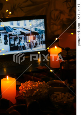 Movie on laptop at night in bedroom lit with candles. Pop corn. Autumn atmosphere at home Movie on laptop at night in bedroom lit with candles. Pop corn. Autumn atmosphere at home 83124031