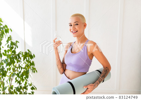 Fitness day. Young fit lady in sportswear holding yoga mat and water in bottle, ready for sport training Fitness day. Young fit lady in sportswear holding yoga mat and water in bottle, ready for sport training 83124749