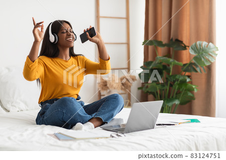 African Lady Listening To Music Wearing Headphones Singing In Bedroom African Lady Listening To Music Wearing Headphones Singing In Bedroom 83124751