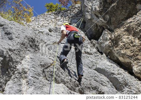Young man climbing natural high rocky wall 83125244