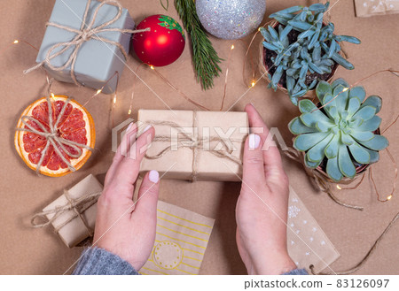 Christmas Gift box wrapped in craft paper in hands of woman Christmas Gift box wrapped in craft paper in hands of woman 83126097