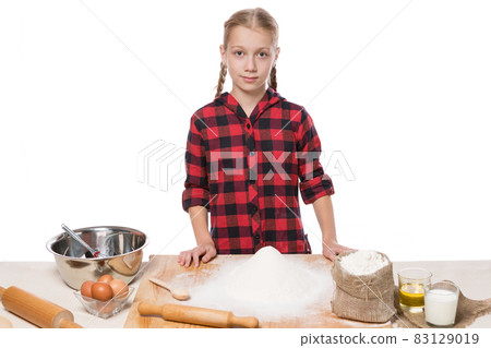 young girl in a red shirt and a lot of ingredients on a table for baking bread or biscuits, on white background, isolate young girl in a red shirt and a lot of ingredients on a table for baking bread or biscuits, on white background, isolate 83129019