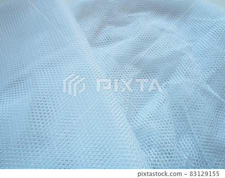 Sheer white net-like tulle. Mesh fabric is wrinkled or folded carelessly. Close-up. White - blue veil or muslin Sheer white net-like tulle. Mesh fabric is wrinkled or folded carelessly. Close-up. White - blue veil or muslin 83129155