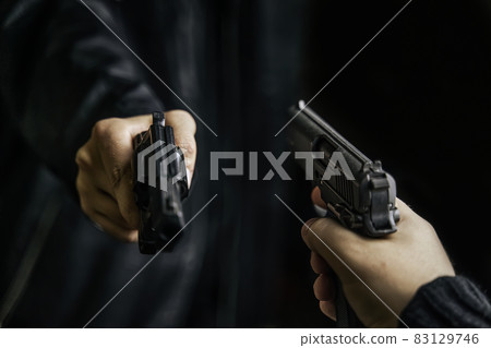 Two men's hands with weapons pointed at each other. 83129746