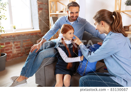 Full-length image of happy smiling family, father and mother, preparing little girl for school. Packing backpack Full-length image of happy smiling family, father and mother, preparing little girl for school. Packing backpack 83130087
