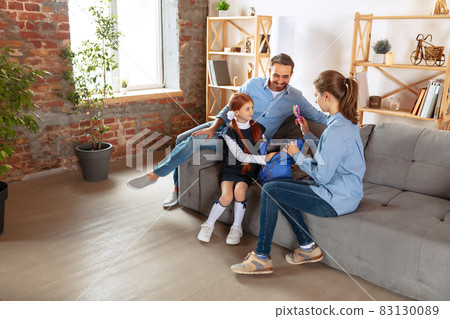 Full-length image of happy family, father and mother, preparing little girl for school. Packing backpack Full-length image of happy family, father and mother, preparing little girl for school. Packing backpack 83130089