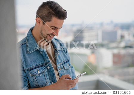Portrait of young caucasian man with smartphone standing on balcony. Portrait of young caucasian man with smartphone standing on balcony. 83131665