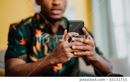 Portrait of unrecognizable young man using smartphone, sitting on sofa at home, social networks concept. 83131733