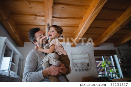 Low angle view of mature father with small daughter having fun indoors at home, holding and hugging. 83131827