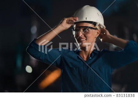 Portrait of mid adult industrial woman working indoors in metal workshop during night shift. 83131838