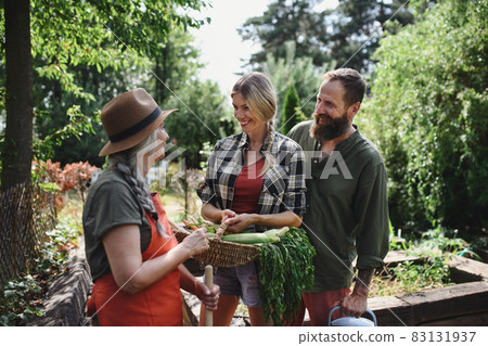 Happy farmers carrying basket with homegrown vegetables outdoors at community farm. 83131937