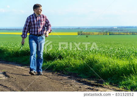 a man as a farmer walking along the field, dressed in a plaid shirt and jeans, checks and inspects young sprouts crops of wheat, barley or rye, or other cereals, a concept of agriculture and agronomy a man as a farmer walking along the field, dressed in a plaid shirt and jeans, checks and inspects young sprouts crops of wheat, barley or rye, or other cereals, a concept of agriculture and agronomy 83132052