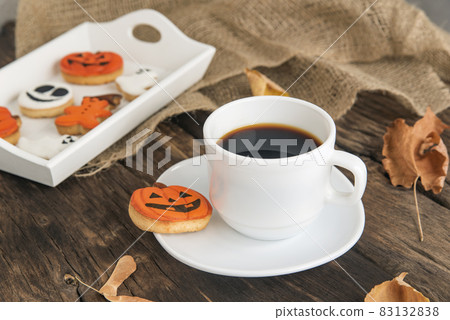 Autumn composition of orange and white cookies for Halloween, cups of fragrant black coffee stands on brown wooden table Autumn composition of orange and white cookies for Halloween, cups of fragrant black coffee stands on brown wooden table 83132838