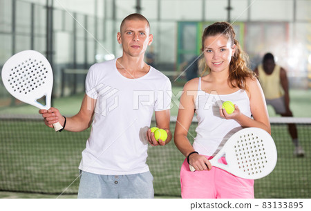 Couple with padel rackets posing on tennis court 83133895