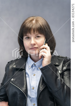 Portrait of stylish young woman in leather jacket with phone in her hands. Vertical frame. 83134271