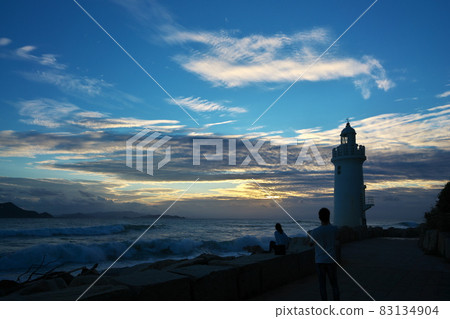 A couple taking a commemorative photo at the Irago Cape Lighthouse in the setting sun 83134904