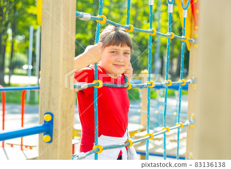 Happy girl climbing on rope ladder on playground 83136138