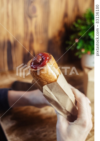 Close-up of a hot dog in hand. The girl has a French manicure. There is a lot of ketchup on top and sauce on the food. The woman wrapped her hands around the bun, creating a hint of intimacy. Close-up of a hot dog in hand. The girl has a French manicure. There is a lot of ketchup on top and sauce on the food. The woman wrapped her hands around the bun, creating a hint of intimacy. 83136180