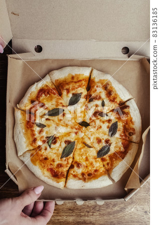 Close-up of Margarita pizza in a disposable dish. Top view of takeaway food in a fast food cafe. On photo - mozzarella cheese, tomatoes, and red basil. The classic recipe. Food for family and friends. Close-up of Margarita pizza in a disposable dish. Top view of takeaway food in a fast food cafe. On photo - mozzarella cheese, tomatoes, and red basil. The classic recipe. Food for family and friends. 83136185
