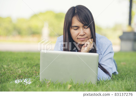 Asian woman lay down green garden park using laptop working outdoor home office. Happiness Woman smile working Freelance on laptop. Young Women University student type computer laptop at green nature 83137276