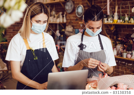 Flower shop workers in protective masks using laptop. Flower shop workers in protective masks using laptop. 83138358