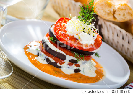 Tasty stack of fried eggplants and tomatoes on spicy sauce served at plate 83138558