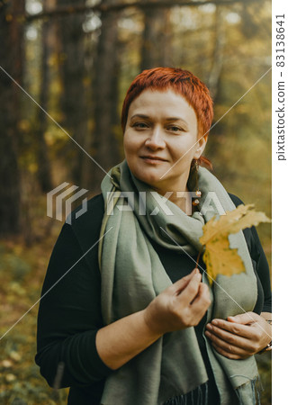 Smiling middle-aged woman 30-40 years old walks in the autumn forest Smiling middle-aged woman 30-40 years old walks in the autumn forest 83138641