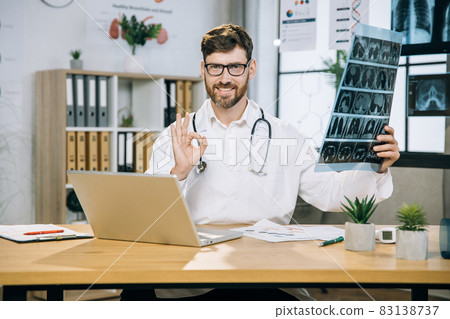 Pleasant 35-aged man scientist sitting at desk with x ray scan in hands Pleasant 35-aged man scientist sitting at desk with x ray scan in hands 83138737