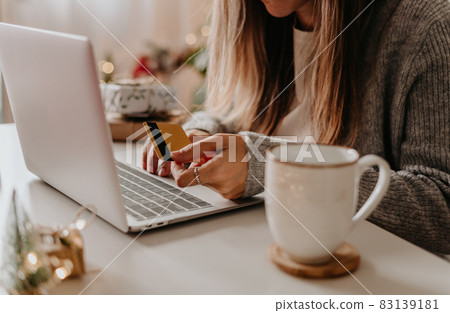 Close up of woman hands with credit card, gifts, coffee cup and laptop. Online shopping at Christmas holidays. Freelance girl woking from home office. Close up of woman hands with credit card, gifts, coffee cup and laptop. Online shopping at Christmas holidays. Freelance girl woking from home office. 83139181