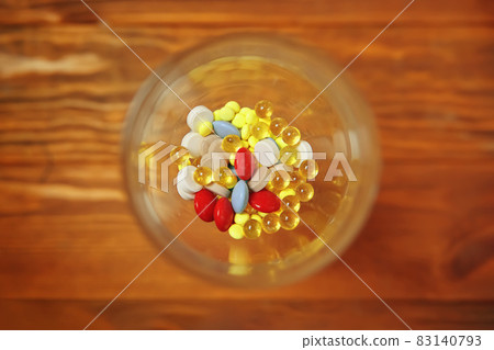 Flat lay of glass with colorful vitamins and pills inside. 83140793