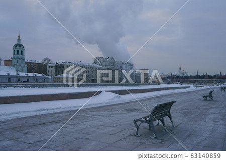Moscow downtown cityscape. Spasskaya Towers, Ivan the Great Bell Tower, observation deck in Zaryadye park in winter blue sunset over the city. Empty benches on the embankment. It's so cold 83140859