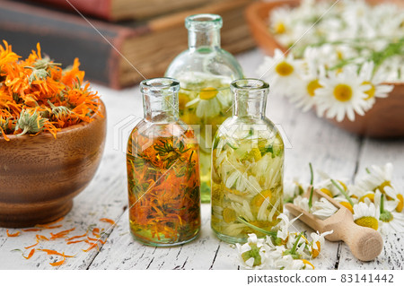 Bottles of chamomile and calendula essential oil or infusion, mortars of dried calendula and daisy flowers, wooden scoop of plucked chamomile flowers. Alternative herbal medicine, aromatherapy. 83141442