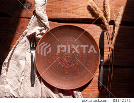 Empty craft handmade clay plate with fork knife on wooden background. Table place hand crafted dish Home interior decor 83142171