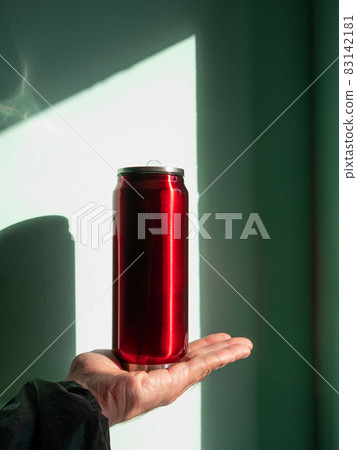 Red thermo can bottle in male hands against wall with harsh shadow.Hot tea coffee drinking in cold autumn winter weather Red thermo can bottle in male hands against wall with harsh shadow.Hot tea coffee drinking in cold autumn winter weather 83142181