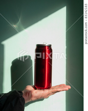 Red thermo can bottle in male hands against wall with harsh shadow.Hot tea coffee drinking in cold autumn winter weather Red thermo can bottle in male hands against wall with harsh shadow.Hot tea coffee drinking in cold autumn winter weather 83142183