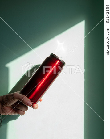 Red thermo can bottle in male hands against wall with harsh shadow.Hot tea coffee drinking in cold autumn winter weather Red thermo can bottle in male hands against wall with harsh shadow.Hot tea coffee drinking in cold autumn winter weather 83142184