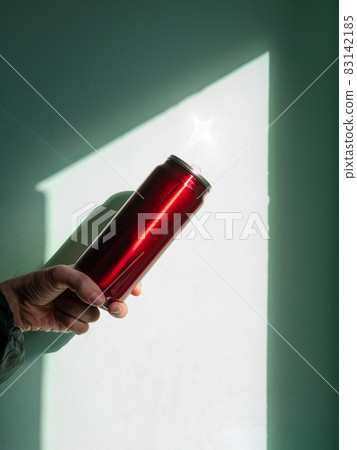 Red thermo can bottle in male hands against wall with harsh shadow.Hot tea coffee drinking in cold autumn winter weather Red thermo can bottle in male hands against wall with harsh shadow.Hot tea coffee drinking in cold autumn winter weather 83142185