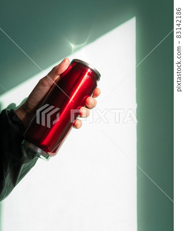 Red thermo can bottle in male hands against wall with harsh shadow.Hot tea coffee drinking in cold autumn winter weather Red thermo can bottle in male hands against wall with harsh shadow.Hot tea coffee drinking in cold autumn winter weather 83142186