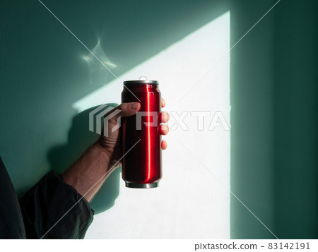 Red thermo can bottle in male hands against wall with harsh shadow.Hot tea coffee drinking in cold autumn winter weather Red thermo can bottle in male hands against wall with harsh shadow.Hot tea coffee drinking in cold autumn winter weather 83142191