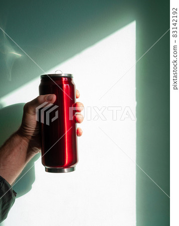 Red thermo can bottle in male hands against wall with harsh shadow.Hot tea coffee drinking in cold autumn winter weather Red thermo can bottle in male hands against wall with harsh shadow.Hot tea coffee drinking in cold autumn winter weather 83142192