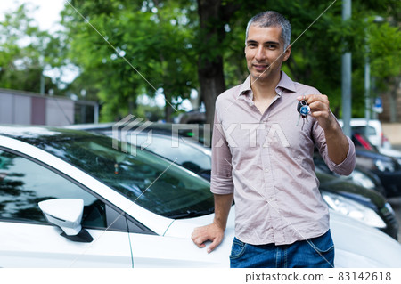 Portrait of male who is standing satisfied with key near his car 83142618