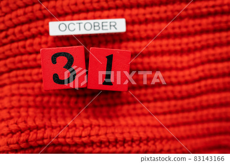 Wooden cube calendar showing October 31, Halloween isolated on red background red knitted sweater. 83143166