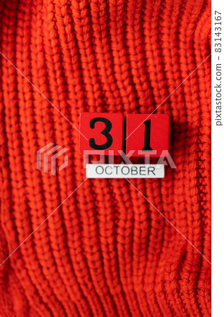 Wooden cube calendar showing October 31, Halloween isolated on red background red knitted sweater. 83143167