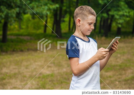 Cute young caucasian kid working with tablet in park. Cute young caucasian kid working with tablet in park. 83143690