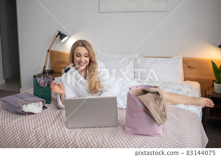 Woman in robe lying on bed near laptop 83144075
