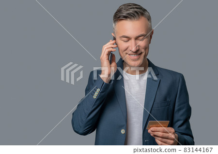 Man with smartphone near ear looking at credit card Man with smartphone near ear looking at credit card 83144167