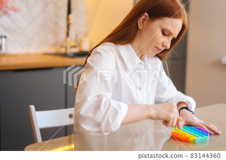 Side view of stressed young woman playing with fidget sensory toy to relieve stress to simple way to be in calm and harmony at home. Side view of stressed young woman playing with fidget sensory toy to relieve stress to simple way to be in calm and harmony at home. 83144360
