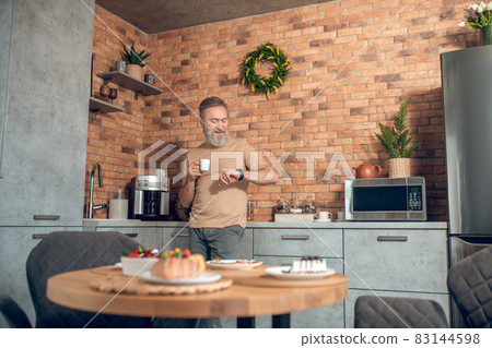 A midagedman standing in the kitchen with a coffee cup in hands A midagedman standing in the kitchen with a coffee cup in hands 83144598